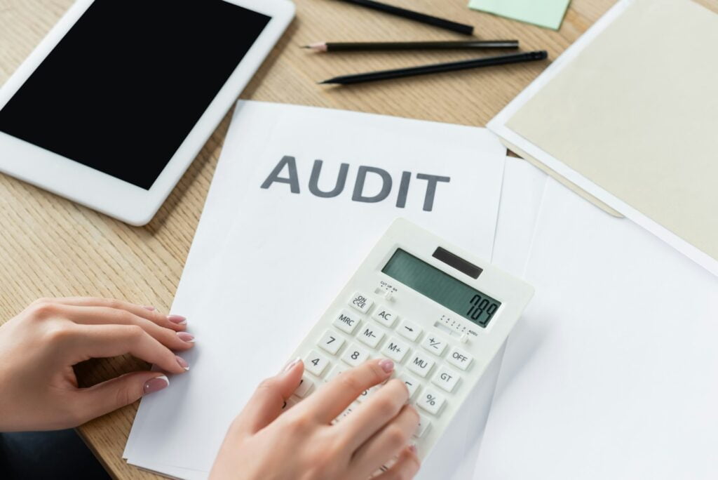 cropped view of tax inspector using calculator near audit document and digital tablet with blank